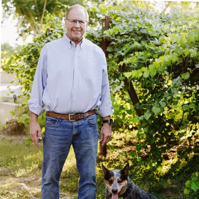 Greg Bohlen, who runs Union Grove Farm, standing beside grapevines with a blue heeler dog at his feet.